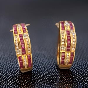 Op de afbeelding: Een paar gouden oorringen met afwisselende rijen vierkant geslepen rode edelstenen en kleine heldere edelstenen. De oorbellen hebben een klassiek, elegant ontwerp.
