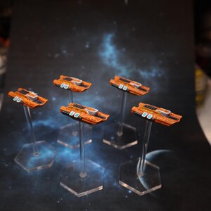 Peut inclure: Cinq vaisseaux spatiaux miniatures orange et noirs sur des supports en plastique transparent. Les vaisseaux spatiaux ont un design bleu et blanc sur le dessus.