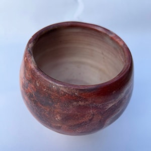 Op de afbeelding: Een kleine, ronde, roodbruine keramische pot met een wit interieur. De pot heeft een gemarmerde, gevlekte uitstraling.