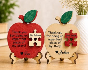 May include: Two wooden apple-shaped plaques with puzzle piece accents. One is red with a tan puzzle piece, the other is tan with a red puzzle piece. Each has text that reads "Thank you for being an important piece of my story!" and a name.