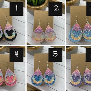 May include: Six pairs of dangle earrings with a layered teardrop design. Each pair features a different color combination of glitter and a silhouette of Mickey Mouse's head. The earrings are numbered 1 through 6.