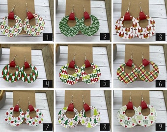 May include: Nine pairs of Christmas themed earrings. Each pair features a different design with red, green, and white colors. The earrings are made of leather and have a circle shape with a hole in the center. The designs include "Joy", "Ho Ho Ho", "Peace", and "Santa".
