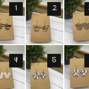 May include: Six pairs of dangle earrings with a Mickey Mouse head design. The earrings are made of cork and feature different animal print patterns, including zebra, leopard, and cheetah.