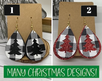 May include: Two pairs of dangle earrings with a black and white buffalo plaid pattern and a black Christmas tree cutout. The second pair has a red glitter Christmas tree cutout.