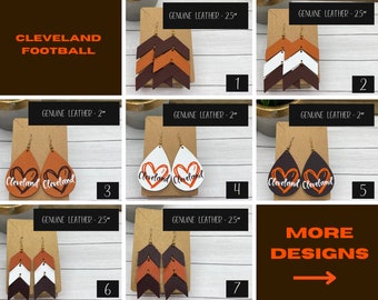 May include: A collection of seven genuine leather earring sets labeled Cleveland Football. Designs include chevron-shaped layers and teardrop shapes with heart graphics and the text Cleveland. Sizes are marked as 2 inches or 2.5 inches in length.