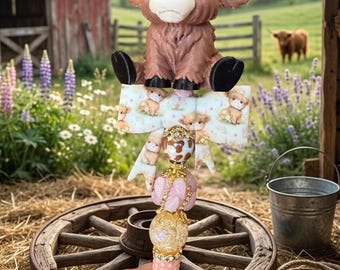 May include: A decorative pen featuring a brown Highland cow figurine with white horns at the top, positioned above a patterned bow with small cow illustrations, followed by a series of gold-accented beads in pink and white cow-print patterns.