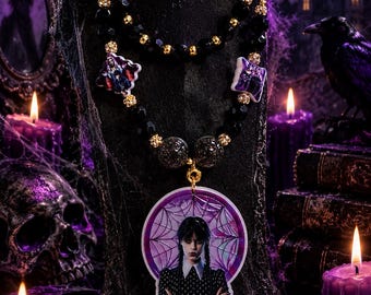 May include: A beaded necklace featuring a large circular pendant with an illustration of a girl with braided hair in a black dress. The necklace includes black and gold beads, two smaller square charms, and gold-toned circular clasps.