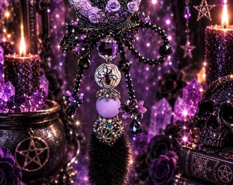 May include: A decorative wand featuring a crescent moon topper with a witch figure and purple roses. The handle includes a spiderweb bead, a solid purple sphere, a textured metallic bead, and a black faux fur pom-pom accent with dangling black beads.