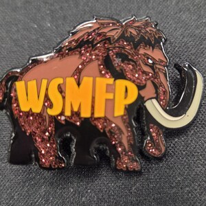 May include: A metal enamel pin shaped like a woolly mammoth with brown glittery fur, black outlines, and large curved cream-colored tusks. The letters WSMFP are printed in bold yellow across the side of the mammoth's body in a sans-serif font.