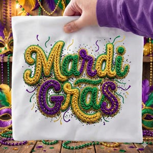 May include: White square pillow with the words "Mardi Gras" embroidered in gold, green, and purple. The design includes decorative sequins and confetti, evoking a festive atmosphere. The pillow is held by a person.