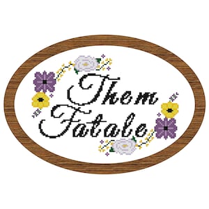 May include: A white oval embroidery hoop with a brown wooden frame. The embroidery features a floral design with purple and yellow flowers and white roses. The text "Them Fatale" is embroidered in black cursive lettering.