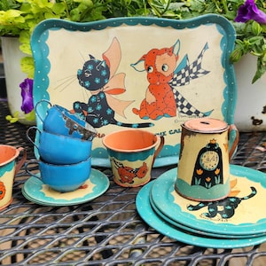 May include: Vintage children's tea set with a tray, cups, saucers, and a small container. The set features illustrations of a cat and dog with wings, and a clock. The color scheme includes blue, orange, and yellow.