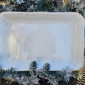 May include: White rectangular serving dish with a decorative scalloped edge. The dish is made of ceramic and has a glossy finish.