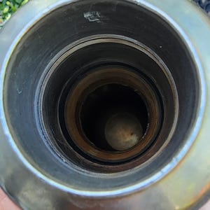 May include: Close-up view of the interior of a metal object, possibly a container or vessel. The object has a circular opening with concentric rings and a dark interior. The metal has a shiny, reflective surface.