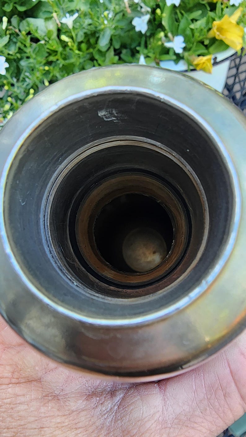 May include: Close-up view of the interior of a metal object, possibly a container or vessel. The object has a circular opening with concentric rings and a dark interior. The metal has a shiny, reflective surface.
