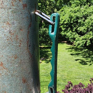 May include: Close-up of a vintage, weathered metal container with a green handle. The container has a textured, teal finish with rust spots. The handle is a dark green color and has a ridged design. The container is outdoors.