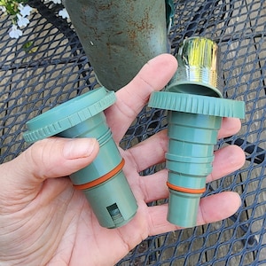May include: Two green replacement stoppers for a vintage Aladdin Stanley thermos. The stoppers have an orange rubber seal and a ridged design. The thermos is visible in the background, with the Aladdin Stanley logo.