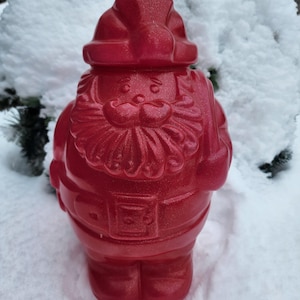 May include: A red plastic Santa Claus figurine with a sparkly finish. The figurine is standing in the snow.