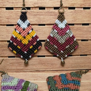 May include: Four pairs of colourful diamond-shaped earrings with intricate woven patterns. The earrings are made with a variety of colours, including red, black, white, brown, green, blue, and orange. The earrings are hanging from silver hooks.