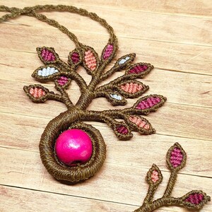 Könnte beinhalten: Eine braune Makramee-Halskette mit einer rosa Holzperle und einem Baumdesign mit rosa, roten und weißen Blättern.