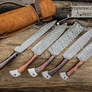 May include: Set of six Damascus steel kitchen knives with wooden handles. The knives are arranged in a row on a wooden surface. The knives are all the same size and have a similar design. The blades are made of Damascus steel and have a wavy pattern. The handles are made of wood and have a dark brown color. The knives are all sharp and have a polished finish. The knives are accompanied by a brown leather knife roll with a strap.