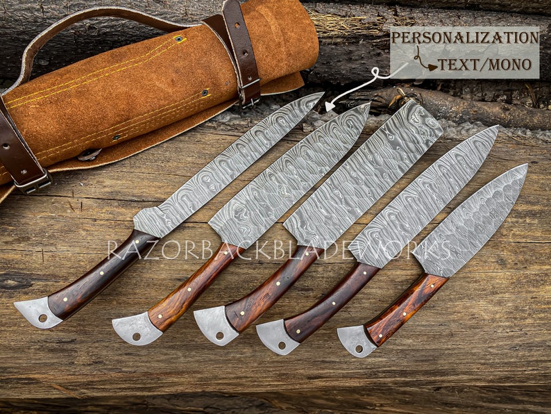 May include: Set of six Damascus steel kitchen knives with wooden handles. The knives are arranged in a row on a wooden surface. The knives are all the same size and have a similar design. The blades are made of Damascus steel and have a wavy pattern. The handles are made of wood and have a dark brown color. The knives are all sharp and have a polished finish. The knives are accompanied by a brown leather knife roll with a strap.
