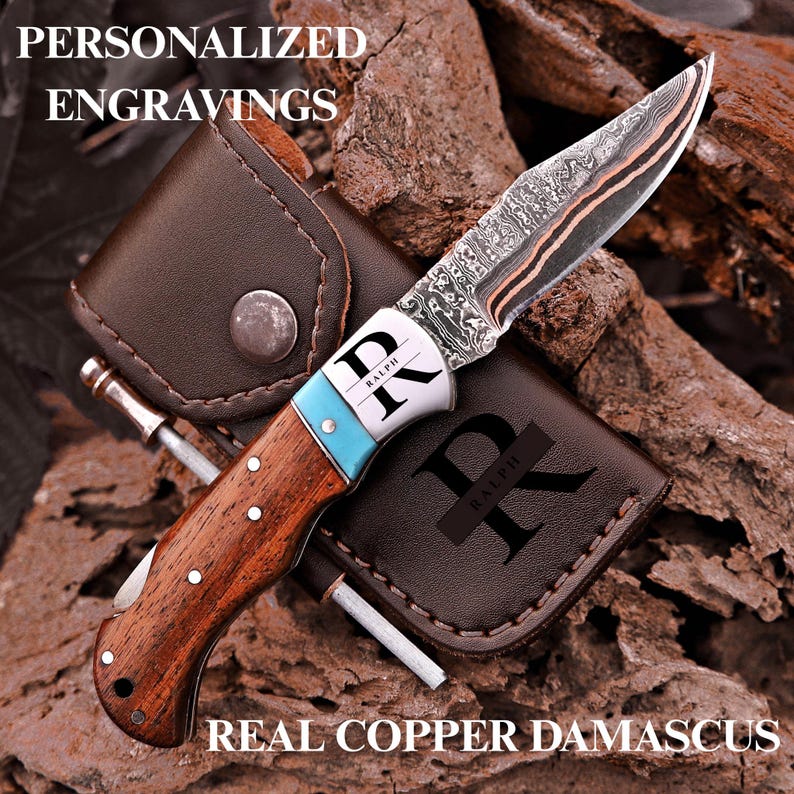 May include: A folding pocket knife with a patterned copper Damascus steel blade, a wooden handle, and a turquoise bolster. The bolster is engraved with the letters "RK" and the name "RALPH". It includes a brown leather sheath with "R" and "RALPH".