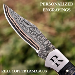 May include: A folding knife with a patterned Damascus steel blade featuring copper layers. The metal bolster is engraved with the letter K and the name Ralph. The text PERSONALIZED ENGRAVINGS and REAL COPPER DAMASCUS appears on the image.