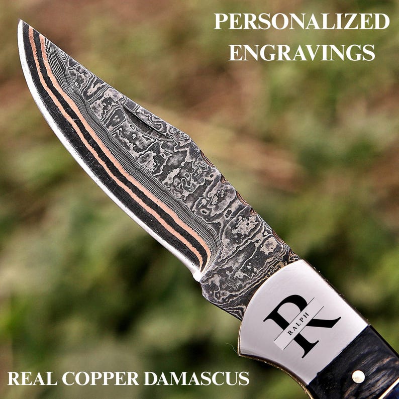 May include: A folding knife with a patterned Damascus steel blade featuring copper layers. The metal bolster is engraved with the letter K and the name Ralph. The text PERSONALIZED ENGRAVINGS and REAL COPPER DAMASCUS appears on the image.