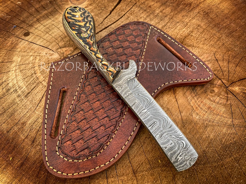 Puede incluir: Un cuchillo artesanal de acero Damasco con mango de madera con patr&oacute;n y funda de cuero. La funda tiene un patr&oacute;n tejido y est&aacute; cosida con hilo marr&oacute;n. El cuchillo est&aacute; apoyado sobre una superficie de madera.