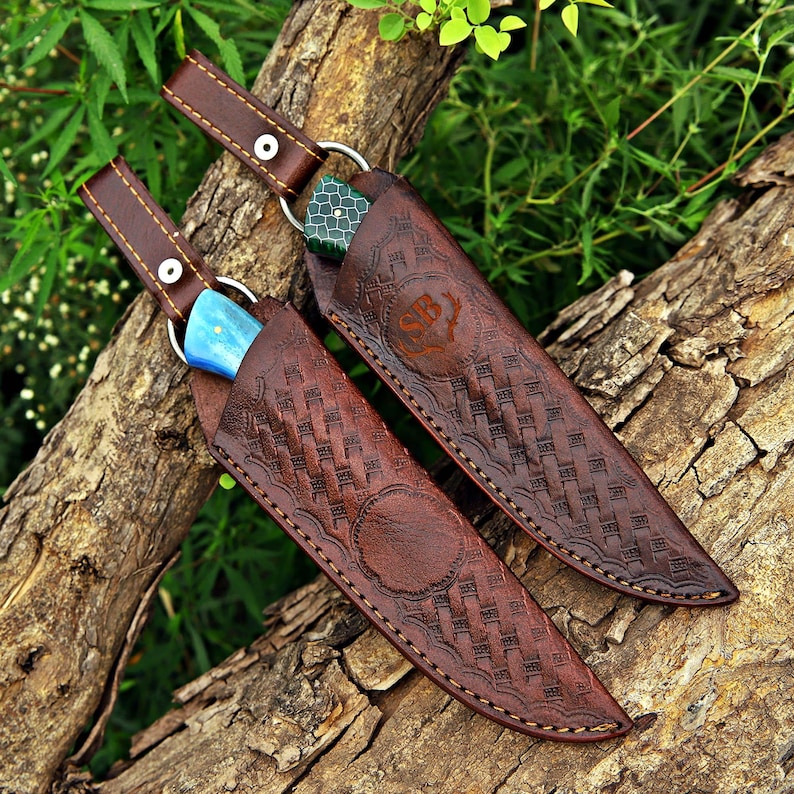 May include: Two knives with patterned brown leather sheaths featuring embossed basket-weave textures and stitching. One knife handle is bright blue, while the other is green with a textured pattern. Each sheath has a strap with a metal snap.