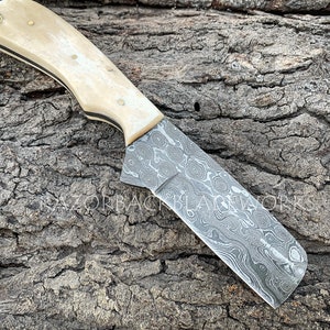 May include: A knife with a white bone handle and a Damascus steel blade. The blade has a wavy pattern and is approximately 7 inches in length.