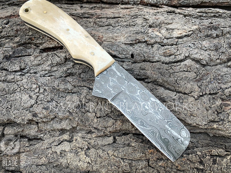 May include: A knife with a white bone handle and a Damascus steel blade. The blade has a wavy pattern and is approximately 7 inches in length.