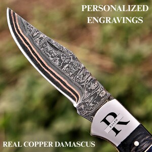May include: A folding knife with a patterned Damascus steel blade featuring copper layers. The metal bolster is engraved with the letter R and the name RALPH. The text PERSONALIZED ENGRAVINGS and REAL COPPER DAMASCUS appears on the image.