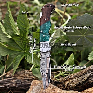 Op de afbeelding: Een zakmes met een 7,62 cm koperen Damascus lemmet, een stalen stootplaat en een 10,16 cm handvat van rozenhout en groene hars. Het mes heeft een vergrendeling en een koordoog, met een totale lengte van 17,78 cm volgens de tekstlabels.