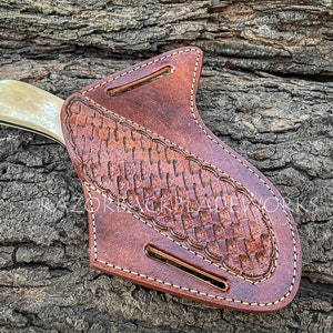 May include: A brown leather knife sheath with a woven pattern and a white handle knife inside. The sheath has a belt loop and a snap closure.