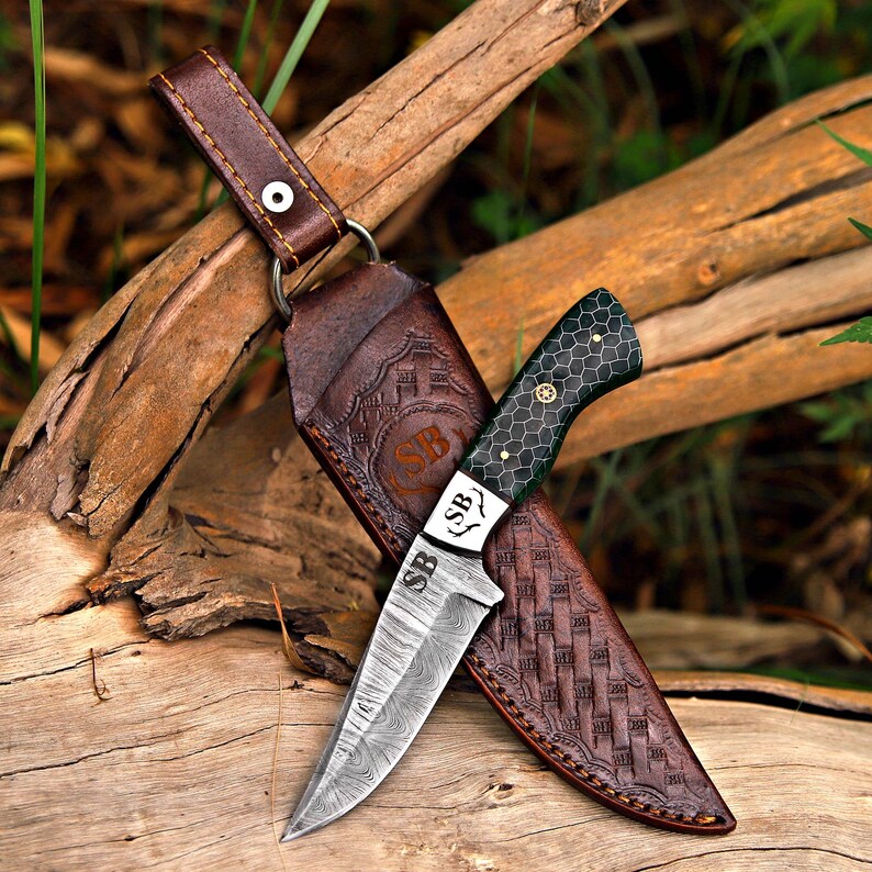 May include: A fixed-blade knife with a Damascus steel blade featuring the letters SB, a dark green handle with a honeycomb pattern, and a brown leather sheath embossed with a basket-weave texture and the letters SB inside a circular emblem.