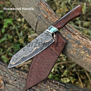 May include: A fixed-blade knife with a patterned Damascus steel blade, a dark brown rosewood handle, and a light blue marbled bolster. The knife includes a brown leather sheath with a textured, cross-hatched pattern and visible stitching.