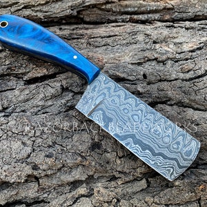 May include: A blue and black patterned chef's knife with a blue wood handle. The knife is on a wooden surface.