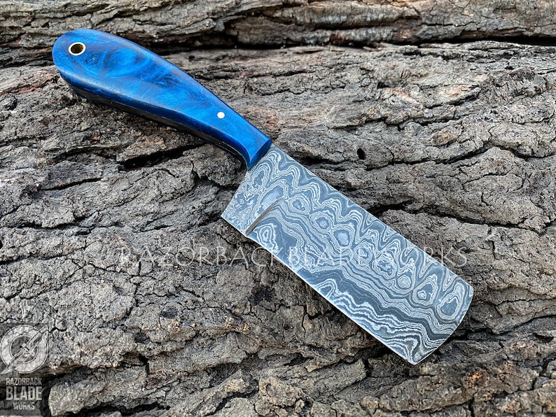 May include: A blue and black patterned chef's knife with a blue wood handle. The knife is on a wooden surface.