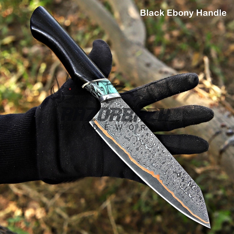 May include: A knife with a black ebony handle and a patterned Damascus steel blade featuring a copper-colored accent line. The bolster is decorated with a turquoise and silver-toned inlay. The text Black Ebony Handle appears at the top right.