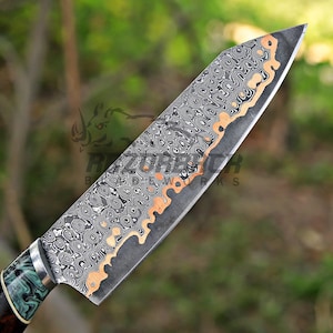 May include: A kitchen knife featuring a blade with a complex, layered Damascus steel pattern in black, gray, and copper tones. The handle is crafted with a marbled green and black resin section, separated from the blade by a silver-colored bolster.