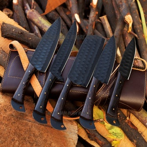 May include: Set of five black chef knives with wooden handles, displayed on a brown leather roll. The knives have a textured, diamond-shaped pattern on the blades.