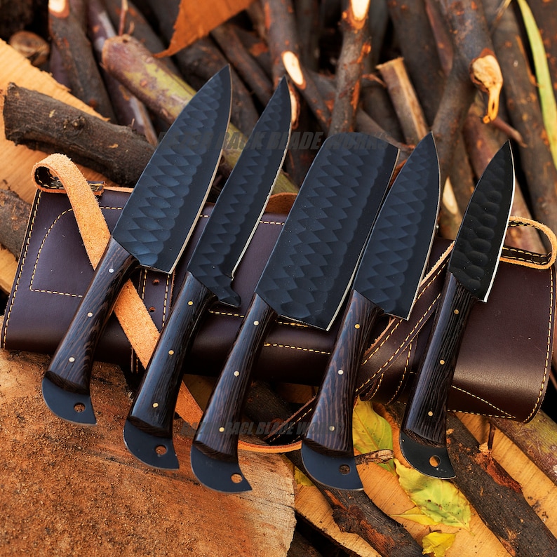 May include: Set of five black chef knives with wooden handles, displayed on a brown leather roll. The knives have a textured, diamond-shaped pattern on the blades.