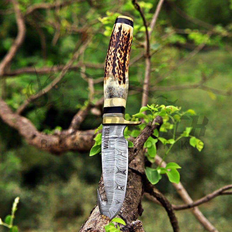 May include: A fixed-blade knife featuring a Damascus steel blade with a gut hook and the word WALTER etched vertically. The handle is crafted from textured brown and cream antler, accented with a brass bolster and a dark spacer near the pommel.