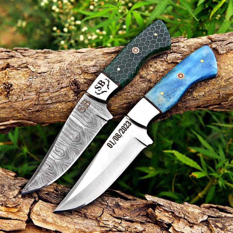 May include: Two knives with metal blades and handles. The top knife has a dark green handle with a honeycomb pattern and a Damascus steel blade engraved with SB. The bottom knife has a blue handle and a smooth blade engraved with 01/08/2023.