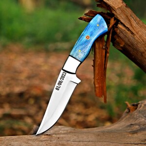 Fixed blade steel skinner knife with personalized engraving and has a colored blue bone handle along with pins and mosaic in center