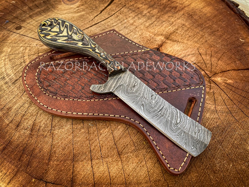 Puede incluir: Una navaja de afeitar recta de acero Damasco con mango de madera y funda de cuero. La navaja tiene un patr&oacute;n &uacute;nico en la hoja y es una hermosa pieza de artesan&iacute;a.