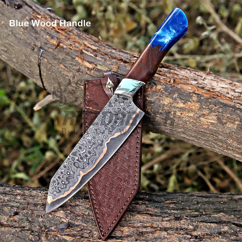 May include: A fixed-blade knife with a patterned Damascus steel blade and a handle made of dark wood and blue resin. The knife is positioned against a brown leather sheath with a textured surface. The text Blue Wood Handle is visible.