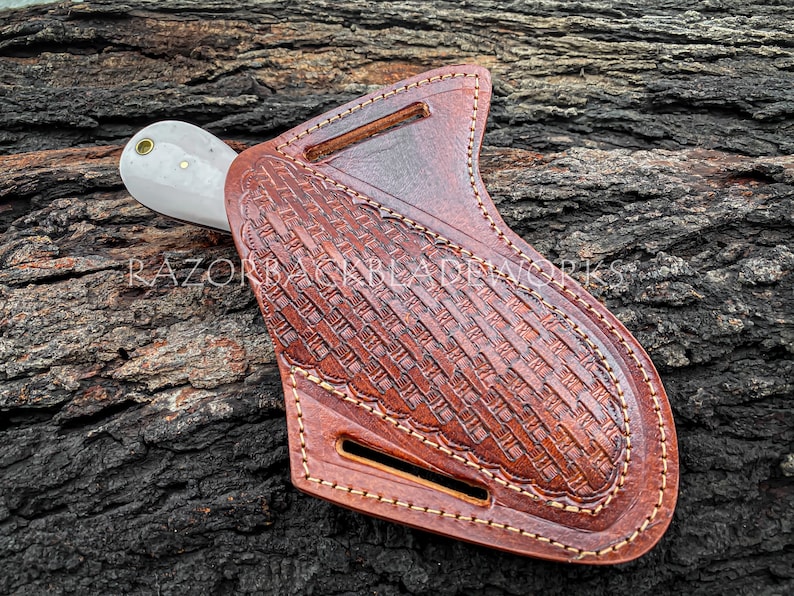 Peut inclure: Un &eacute;tui &agrave; couteau en cuir marron avec un motif tiss&eacute; d&eacute;coratif et des coutures. L'&eacute;tui a une boucle de ceinture et une fermeture &agrave; pression. Le couteau n'est pas inclus.